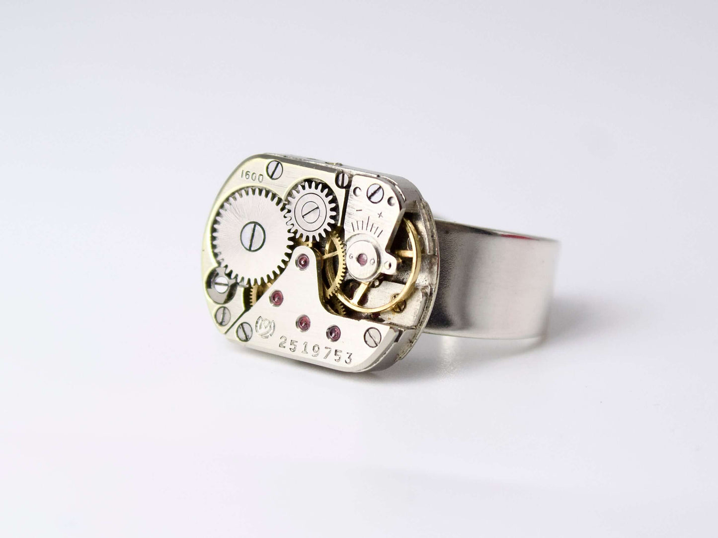 Anello con meccanismo di orologio Glimoire in metallo con ingranaggi visibili su sfondo bianco