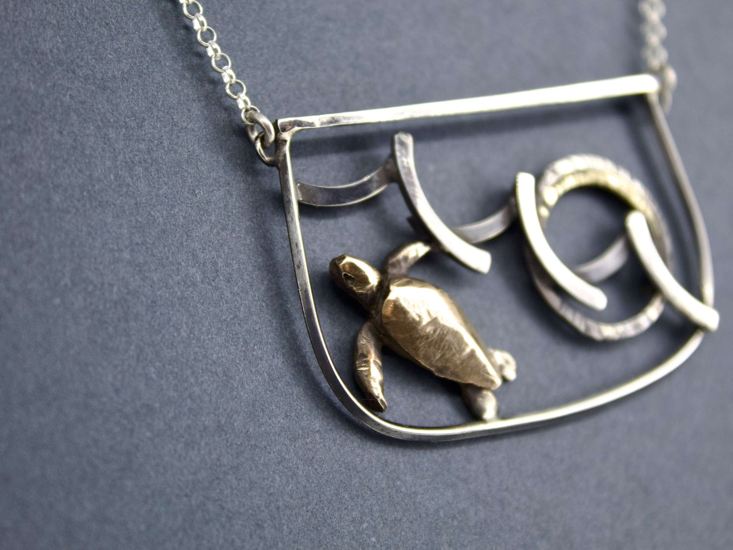 Collana tartaruga incisa a mano di Glimoire con ciondolo in metallo su sfondo grigio