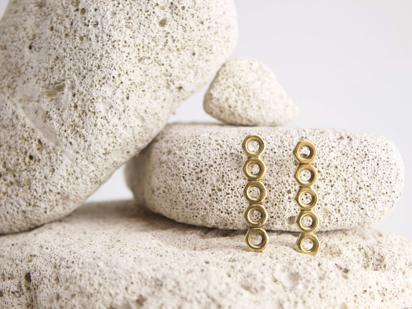 Orecchini esagonali dadini in oro con design elegante su fondo di pietra naturale