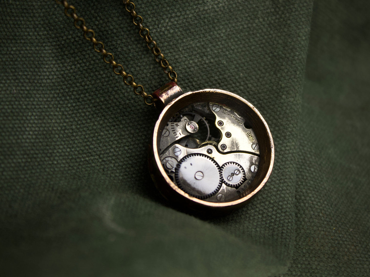 Collana con pendente rotondo in bronzo, contenente meccanismi di orologio con ingranaggi visibili e finitura grezza