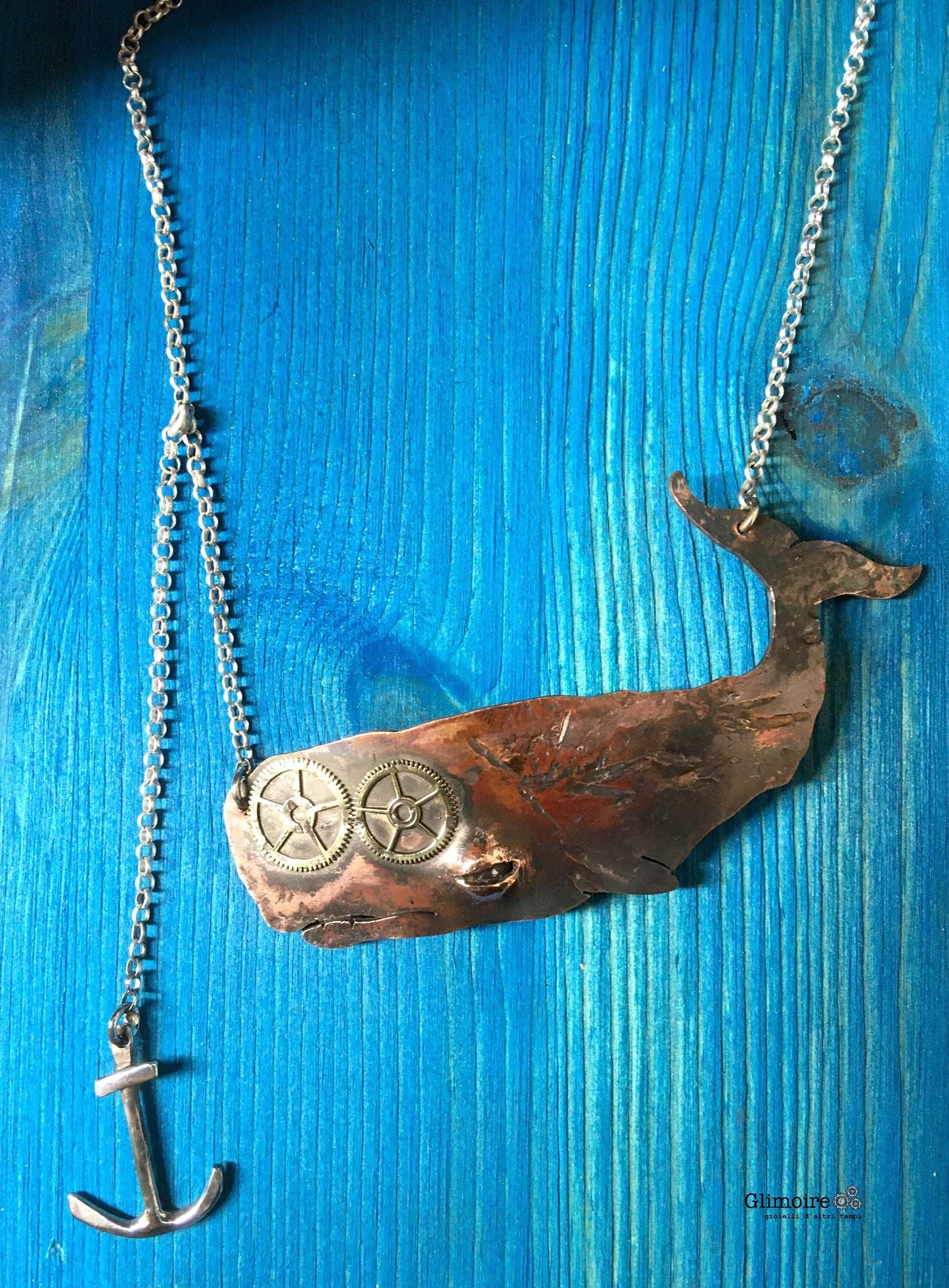 Collana Moby Dick fatta a mano da Glimoire con ciondolo balena e ancora in bronzo su sfondo blu