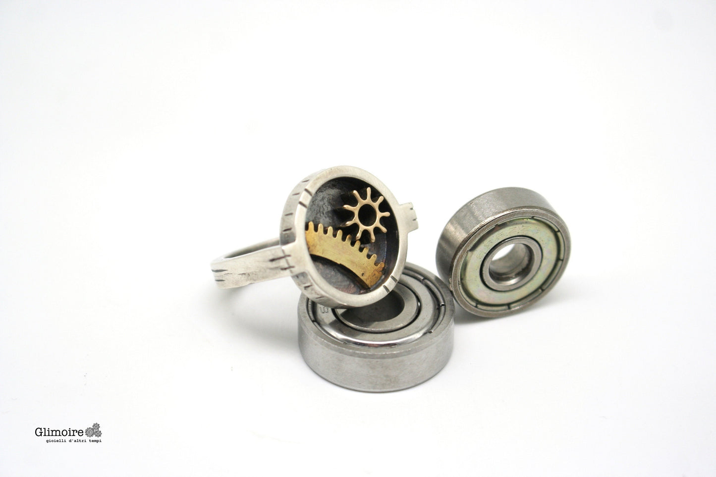 Anello industrial rettangolare Glimoire con ingranaggi metallici su sfondo bianco