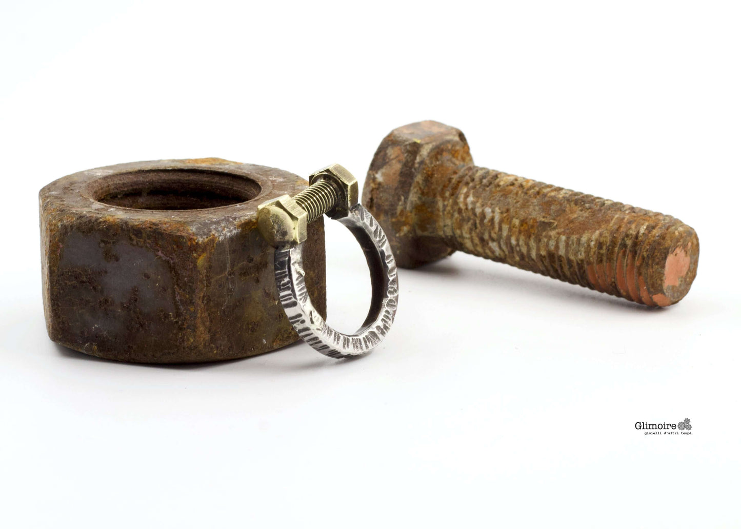 Anello dadi e bulloni Glimoire anello artigianale in metallo vicino a dado e bullone arrugginiti su sfondo bianco
