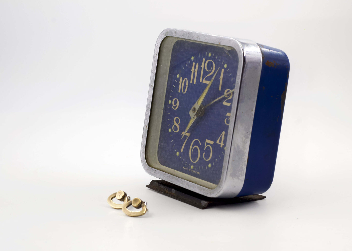 Orecchini particolari ispirati a sveglie con design originale accanto a una sveglia vintage blu