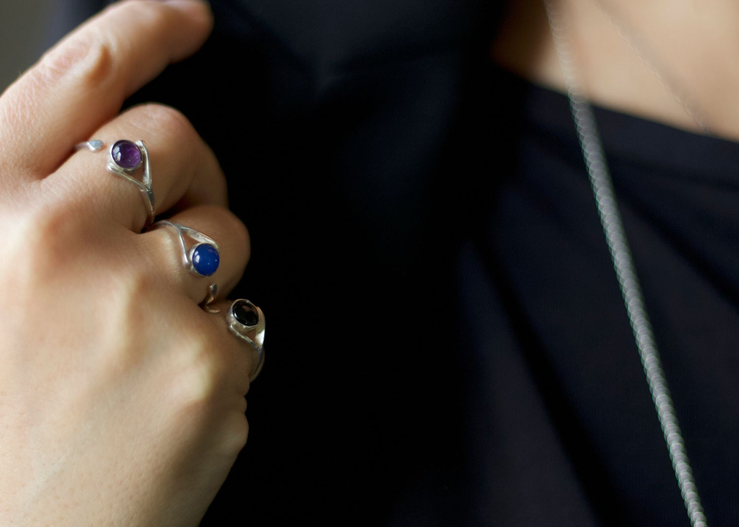 Collezione gioielli con anelli in argento con pietre colorate e collana minimal indossati su abito nero