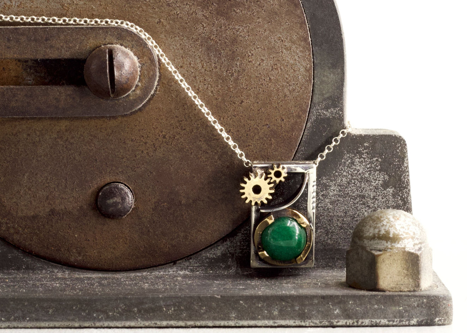 Collezione Gioielli industriali con collana ciondolo a ingranaggio e pietra verde su macchinario metallico rustico