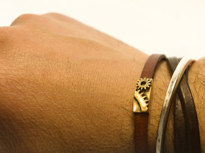 Bracciale industrial con ingranaggi in cuoio e bronzo indossato su un polso maschile