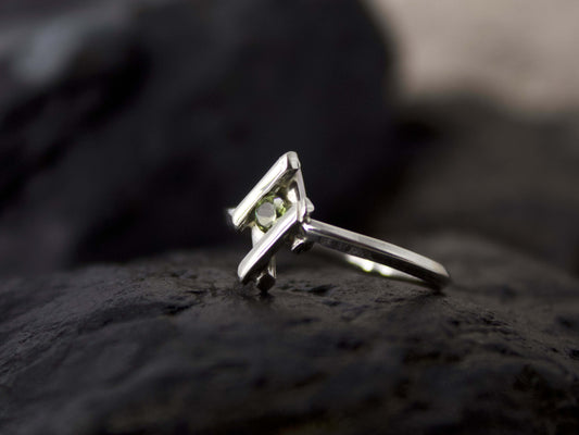 Anellino in argento con pietra verde di Glimoire su sfondo scuro con design moderno