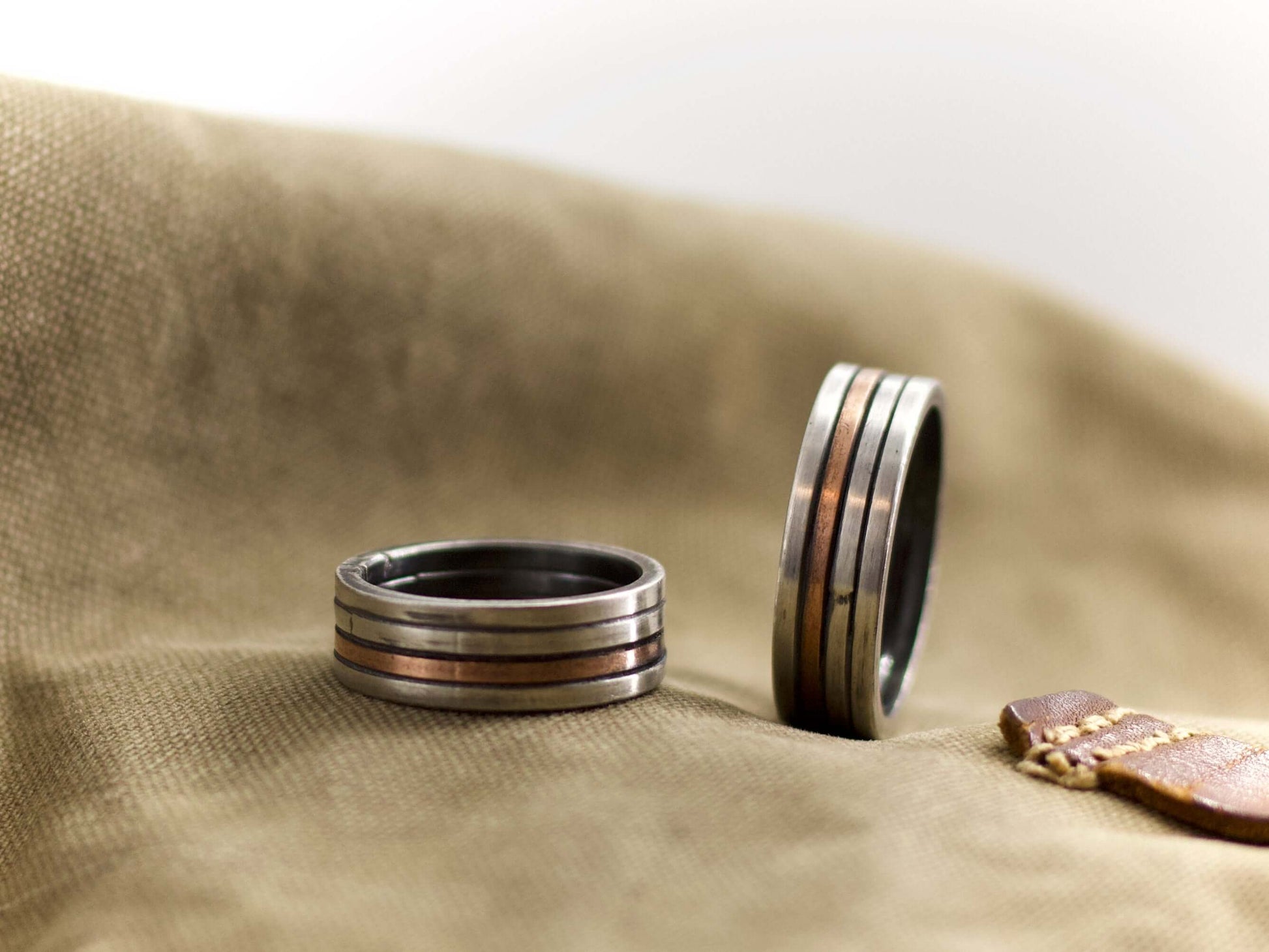 Anello a fascia artigianale uomo Glimoire in metallo con design a strisce su sfondo tessuto marrone
