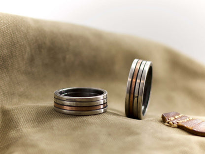 Anello a fascia artigianale uomo Glimoire in metallo con design a strisce su sfondo tessuto marrone