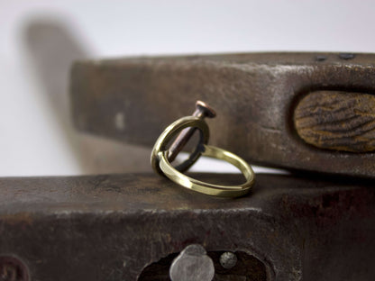 Anello chiodo con anello in ottone e dettagli in rame su sfondo di attrezzi metallici