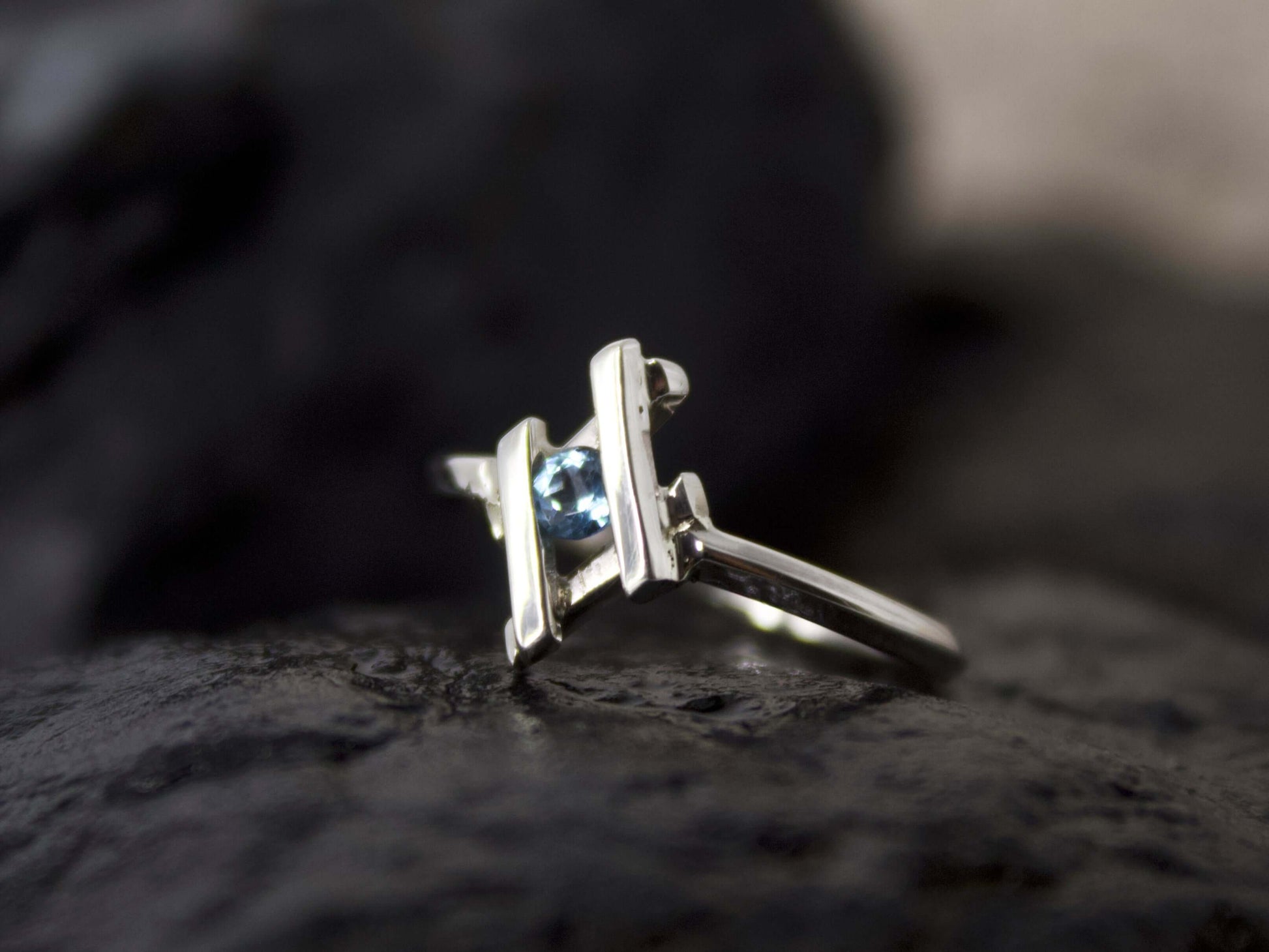 Anello in argento con pietra blu di Glimoire posato su superficie scura con design moderno