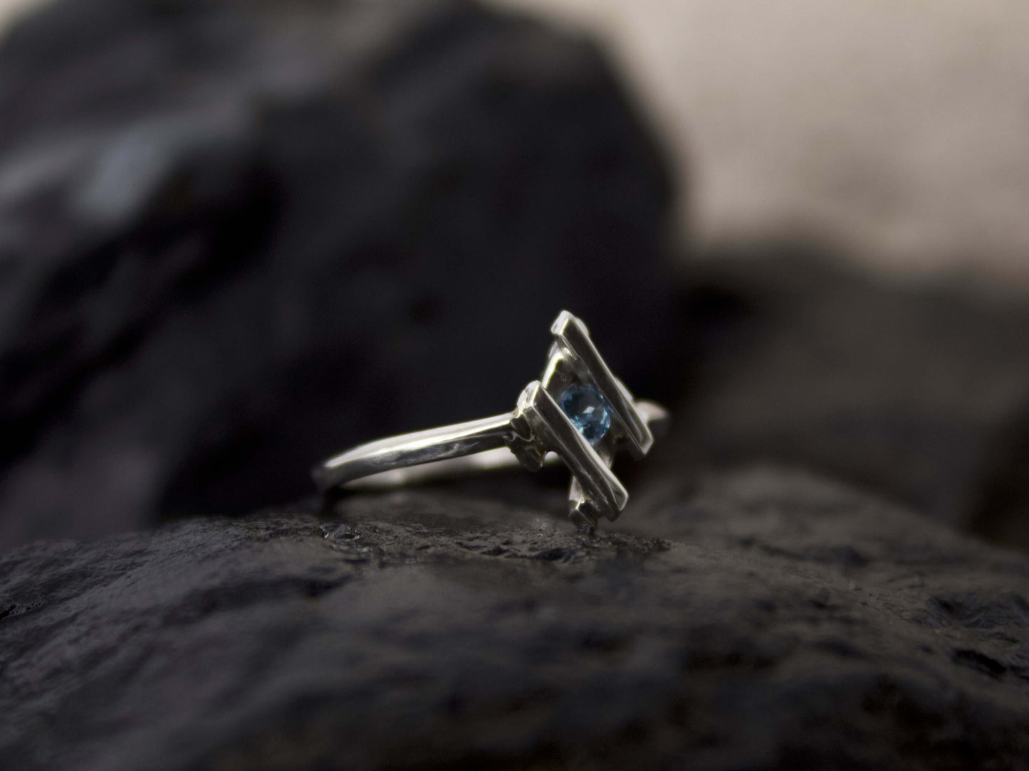 Anello in argento con pietra blu Glimoire posato su superficie scura naturale