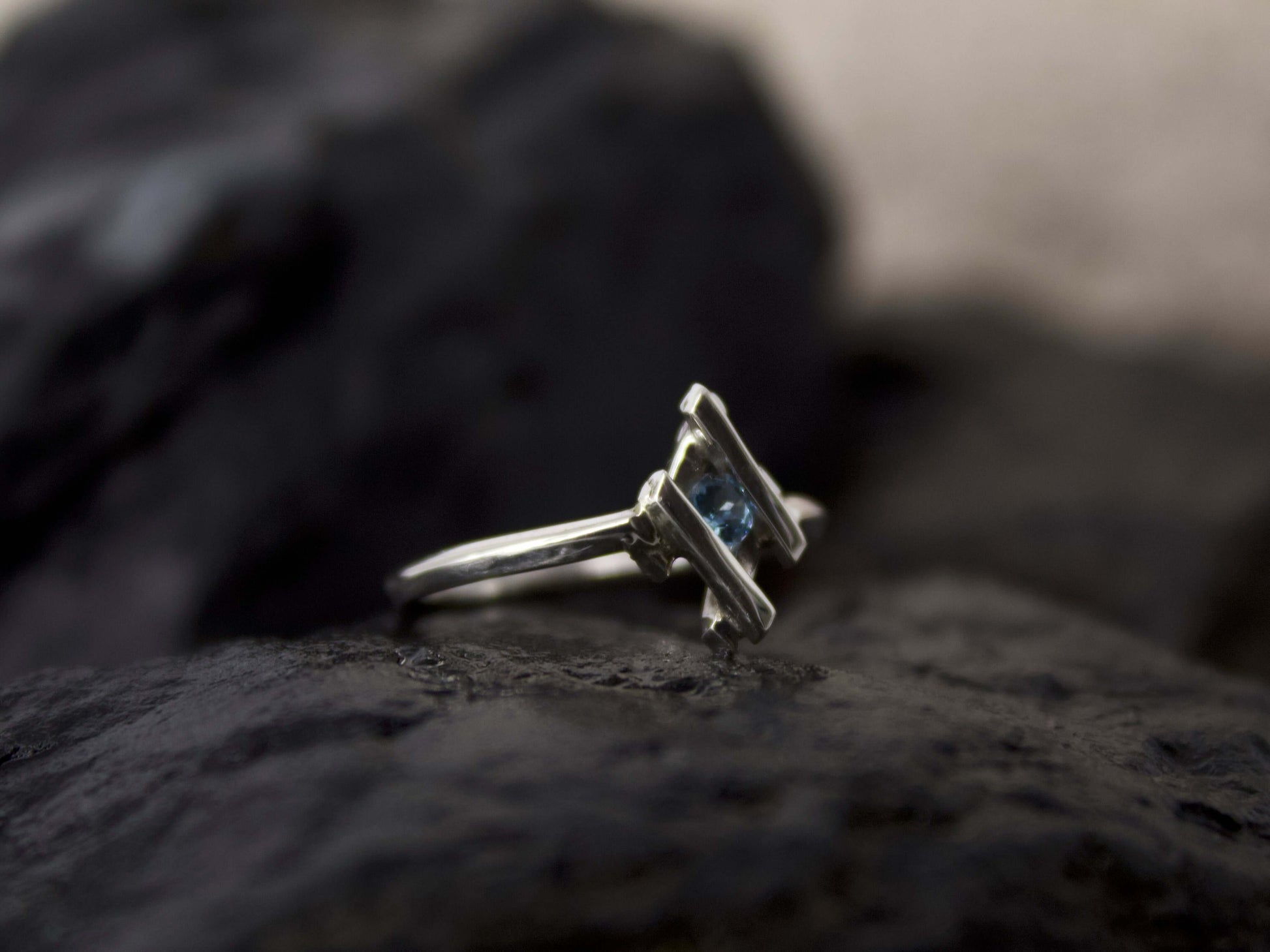 Anello in argento con pietra blu Glimoire posato su superficie scura naturale
