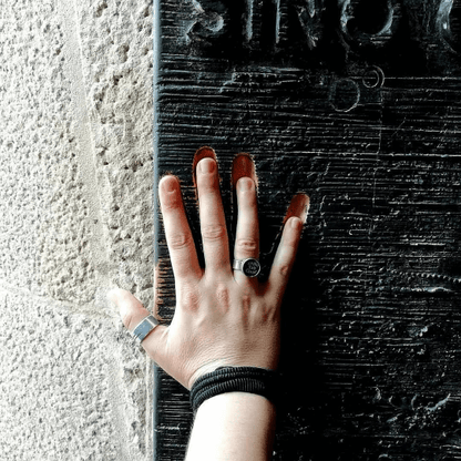 Anello in argento con tasti di macchina da scrivere indossato su mano vicino a muro di pietra