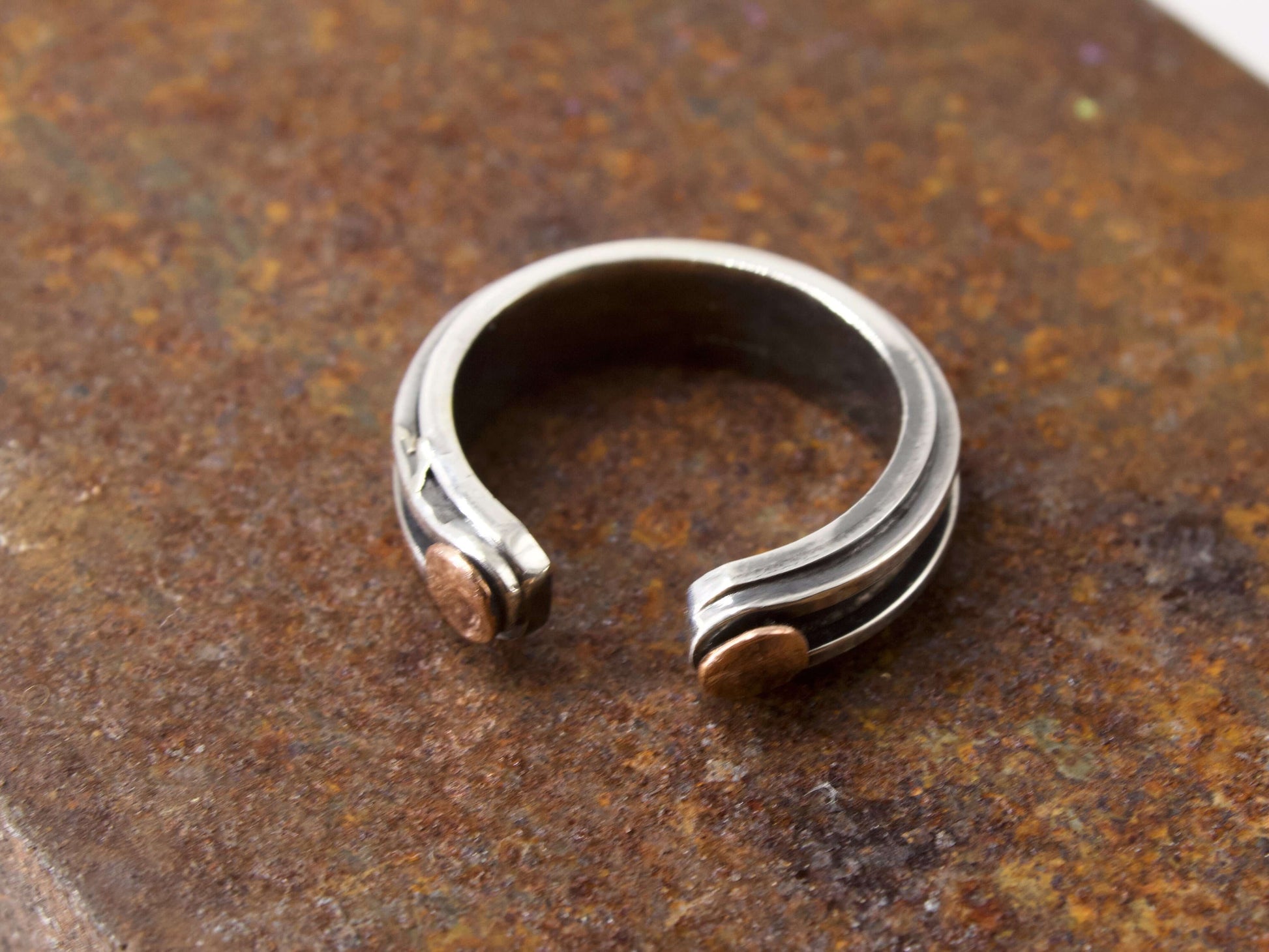 Anello maschile in argento regolabile con dettagli in rame su superficie rugginosa Glimoire