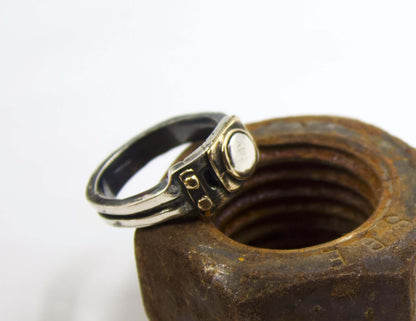 Anello stile industriale uomo Glimoire in metallo con design robusto appoggiato su grande dado arrugginito