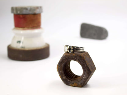 Anello stile industriale uomo Glimoire su dado metallico arrugginito con sfondo sfocato