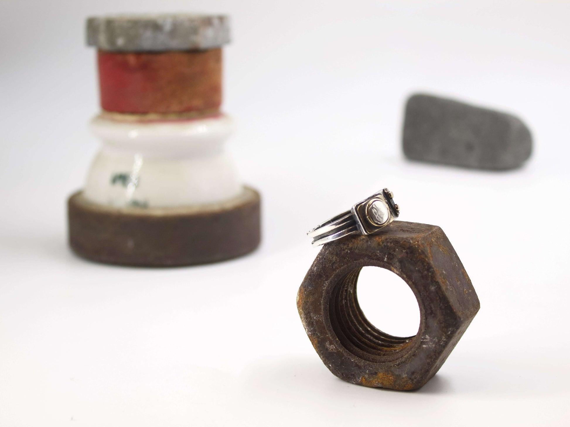 Anello stile industriale uomo Glimoire su dado metallico arrugginito con sfondo sfocato bianco