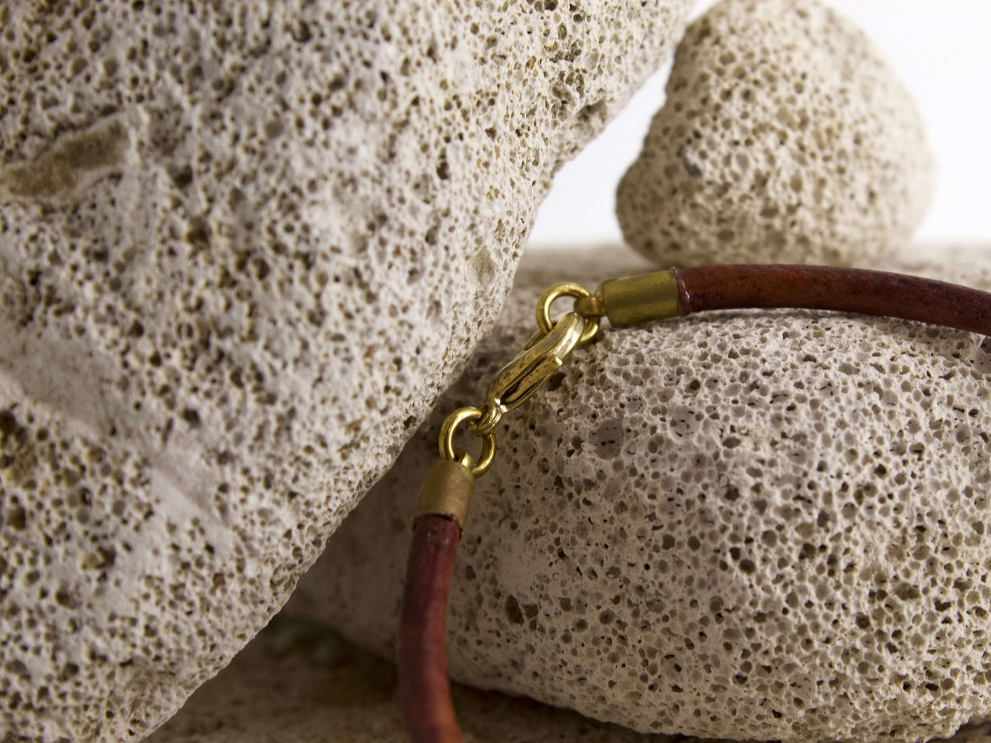 Bracciale in cuoio con dado ottone, visibile con chiusura e dettagli su superfici in pietra