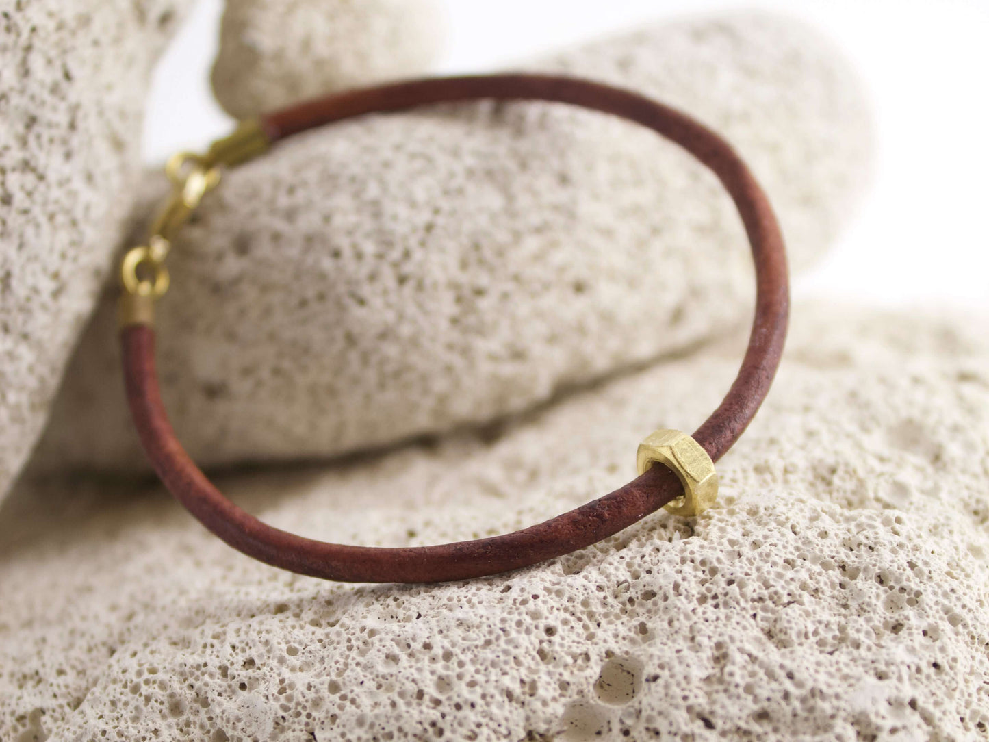 Bracciale in pelle con dado ottone posizionato su una superficie di pietra porosa