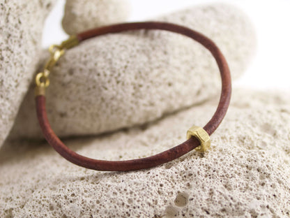 Bracciale in pelle con dado ottone posizionato su una superficie di pietra porosa