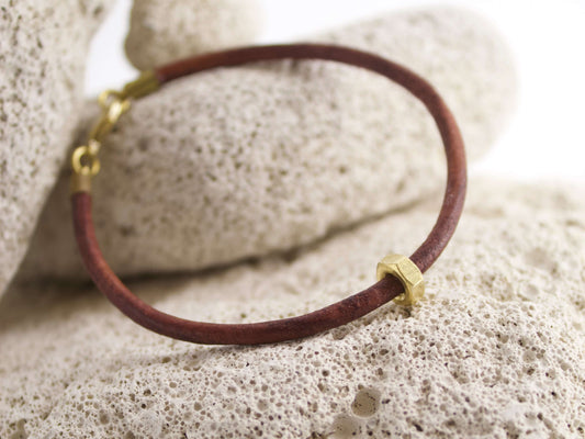 Bracciale in pelle con dado ottone posizionato su una superficie di pietra porosa