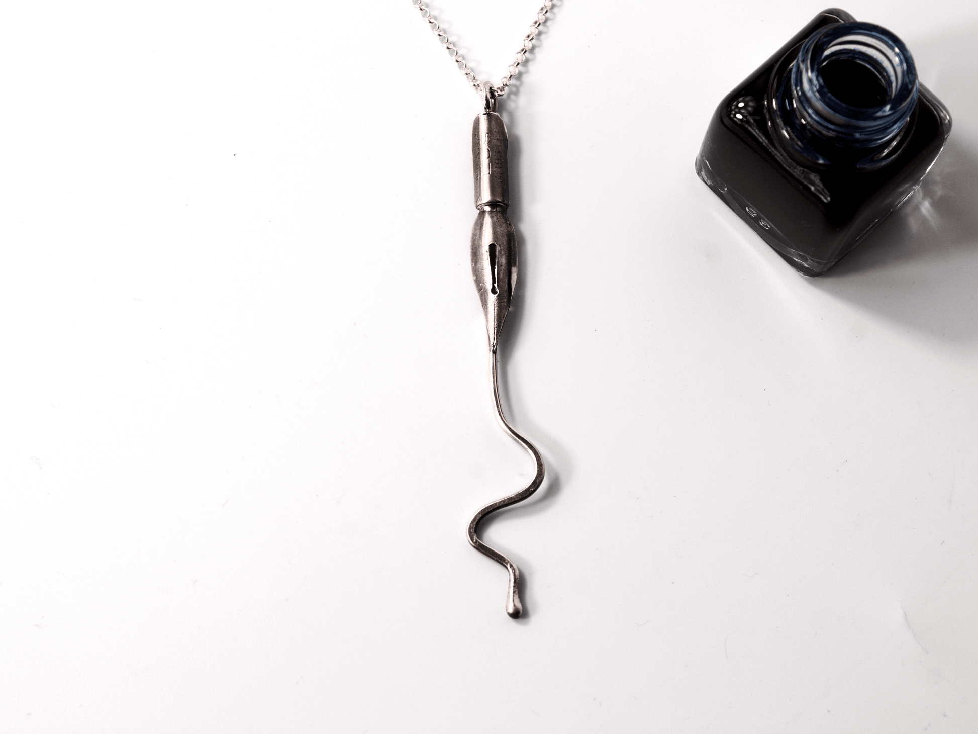 Collana artigianale con ciondolo pennino d'epoca da scrittura accanto a un calamaio nero