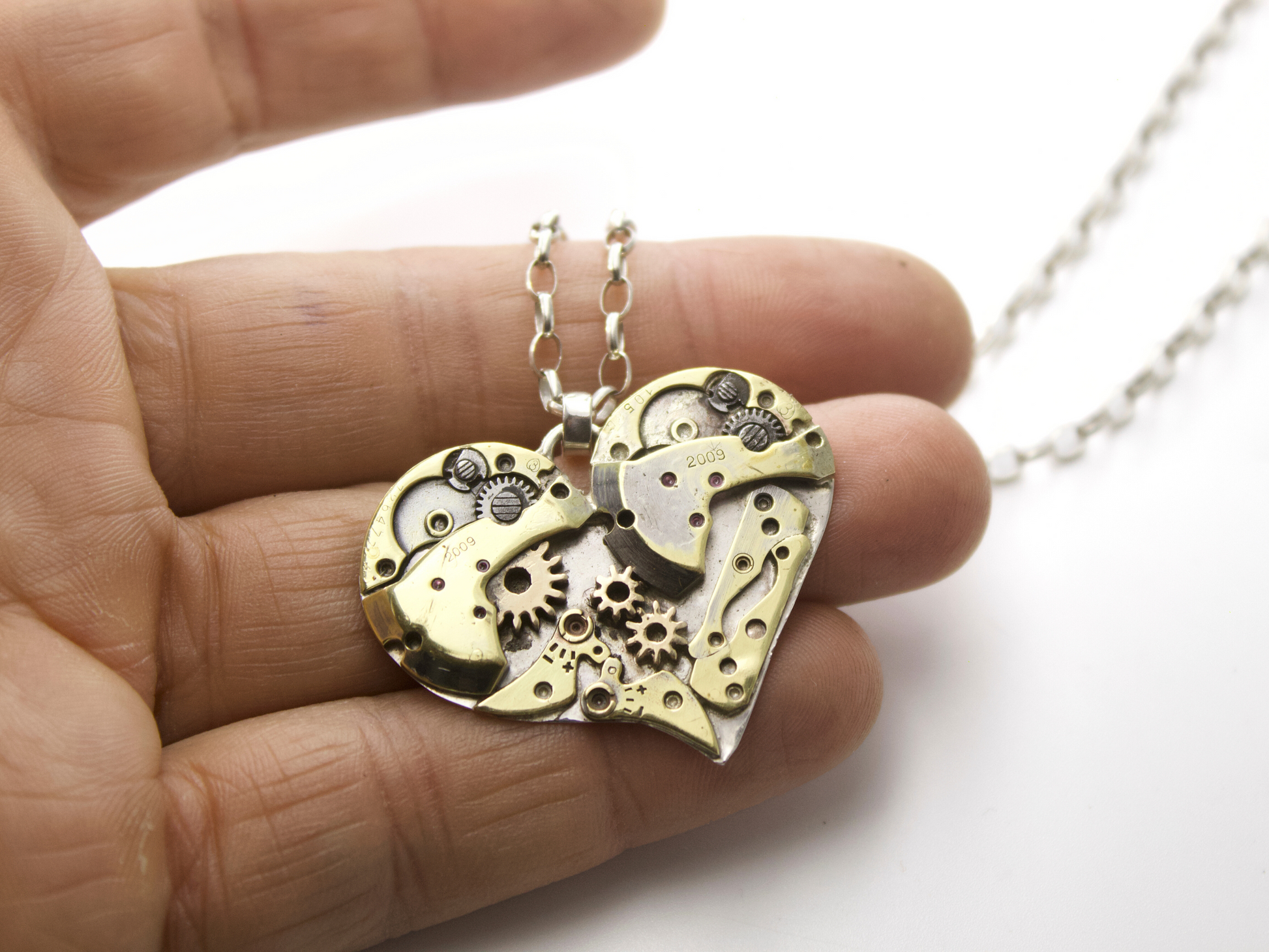 Collana cuore meccanico argento con ingranaggi visibili, tenuta in una mano