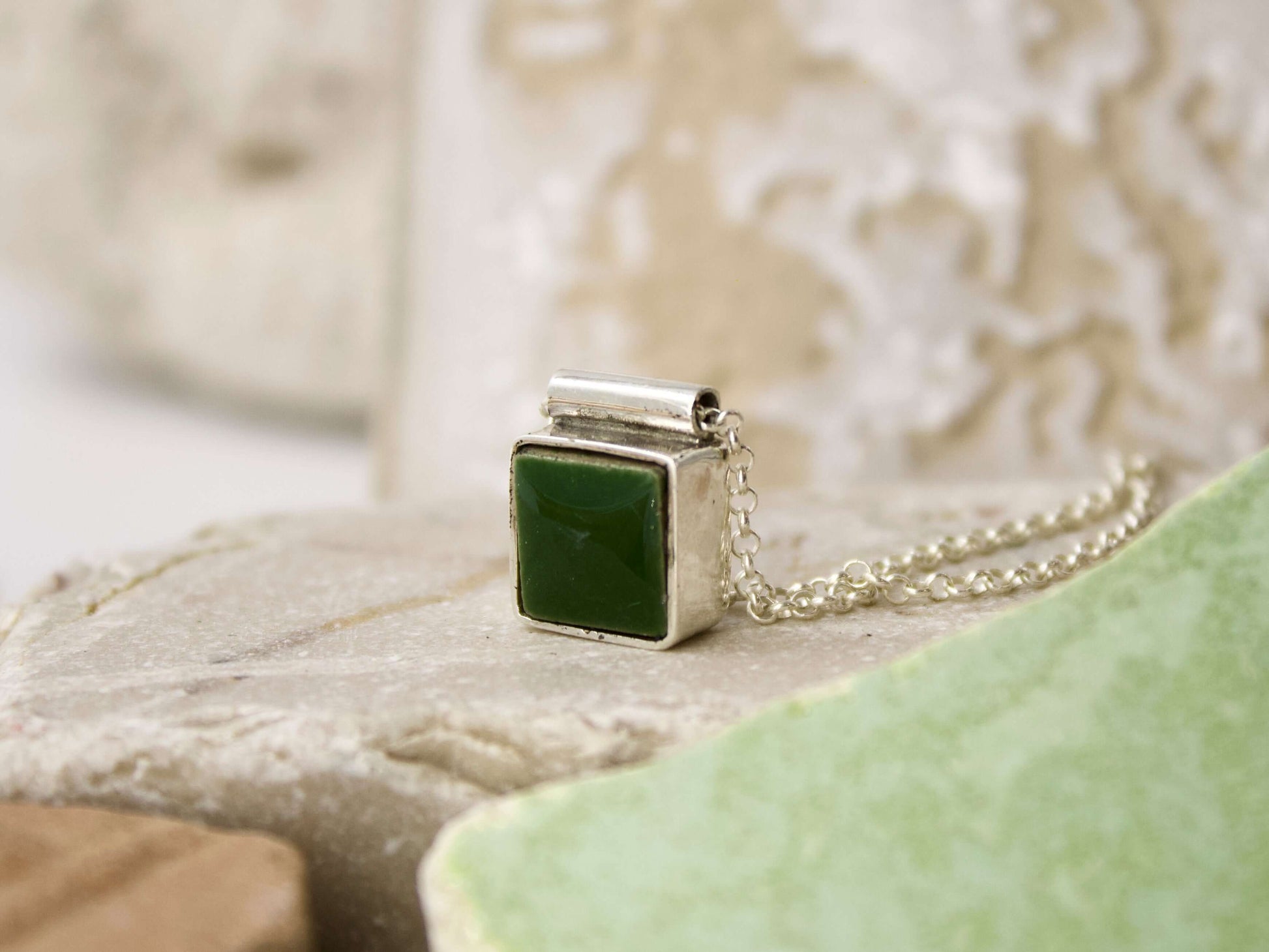 Collana mosaico artigianale con pendente verde in argento fuso su sfondo naturale