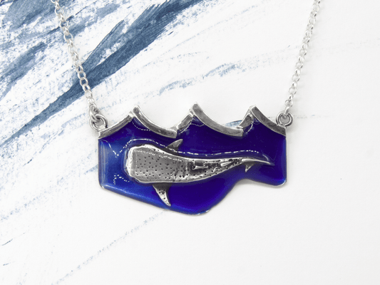 Collana squalobalena Glimoire con ciondolo a forma di balena su sfondo blu e catena argento