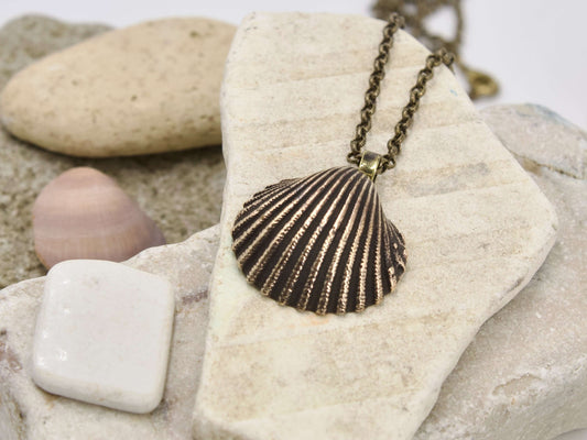 Collana conchiglia vintage in bronzo con catena a maglie di Glimoire su sfondo di pietre naturali