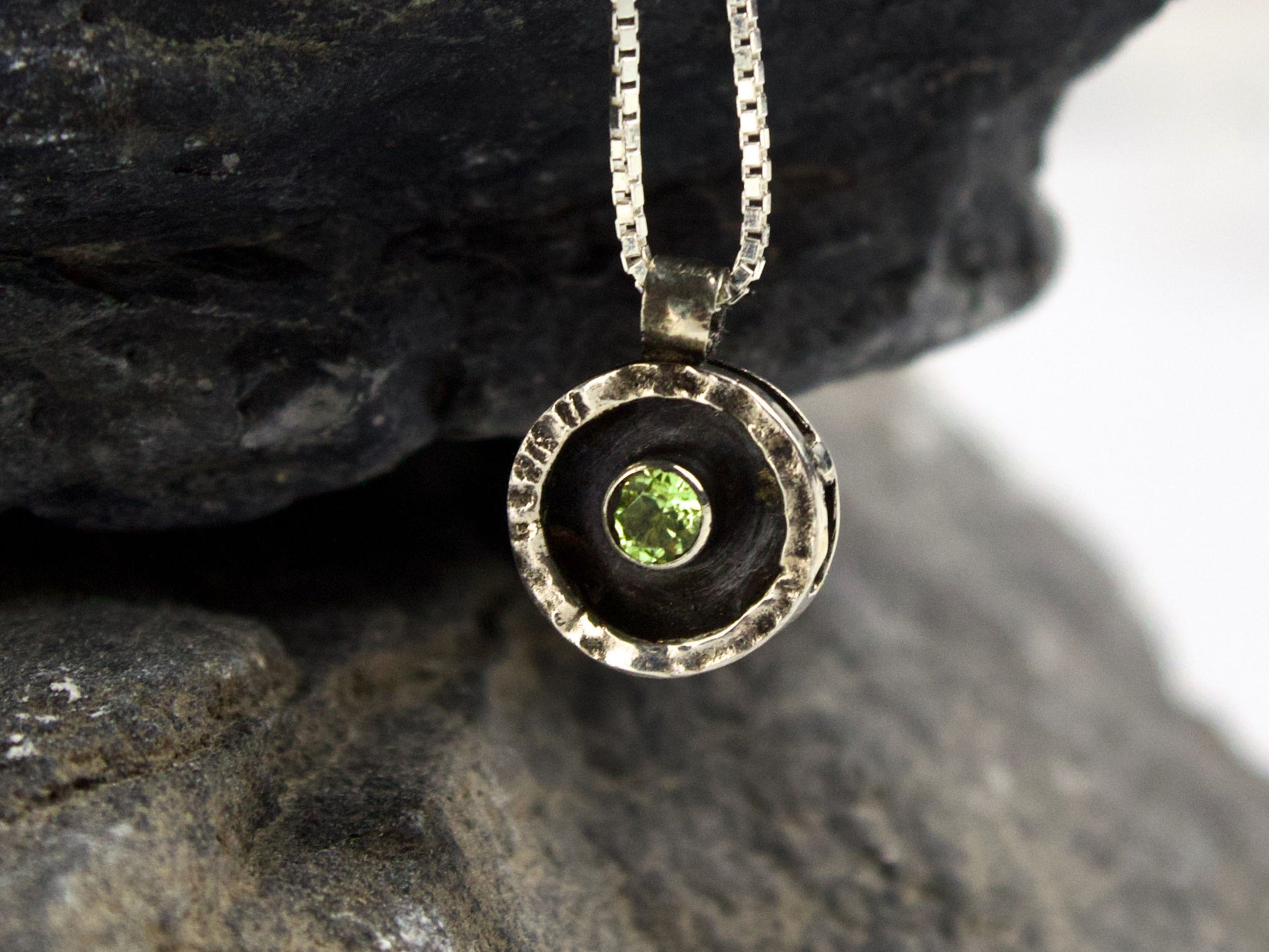 Collana Glimoire con ciondolo circolare in argento e peridoto verde al centro, sospeso in una cornice martellata.