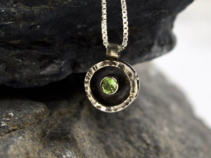 Collana Glimoire con ciondolo circolare in argento e peridoto verde al centro, sospeso in una cornice martellata.
