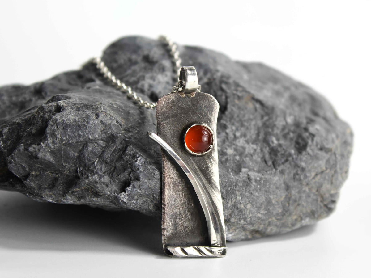 Collana Glimoire con pendente in argento e agata rossa su sfondo di roccia scura