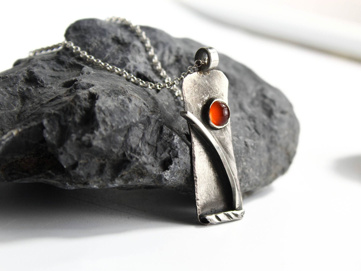 Collana Glimoire con pendant in argento e pietra rossa su una superficie rocciosa