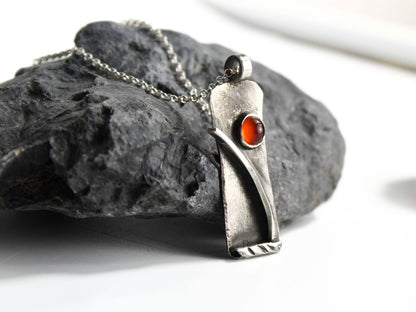 Collana Glimoire con pendant in argento e pietra rossa su una superficie rocciosa