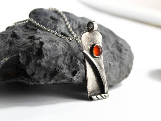 Collana Glimoire con pendant in argento e pietra rossa su una superficie rocciosa