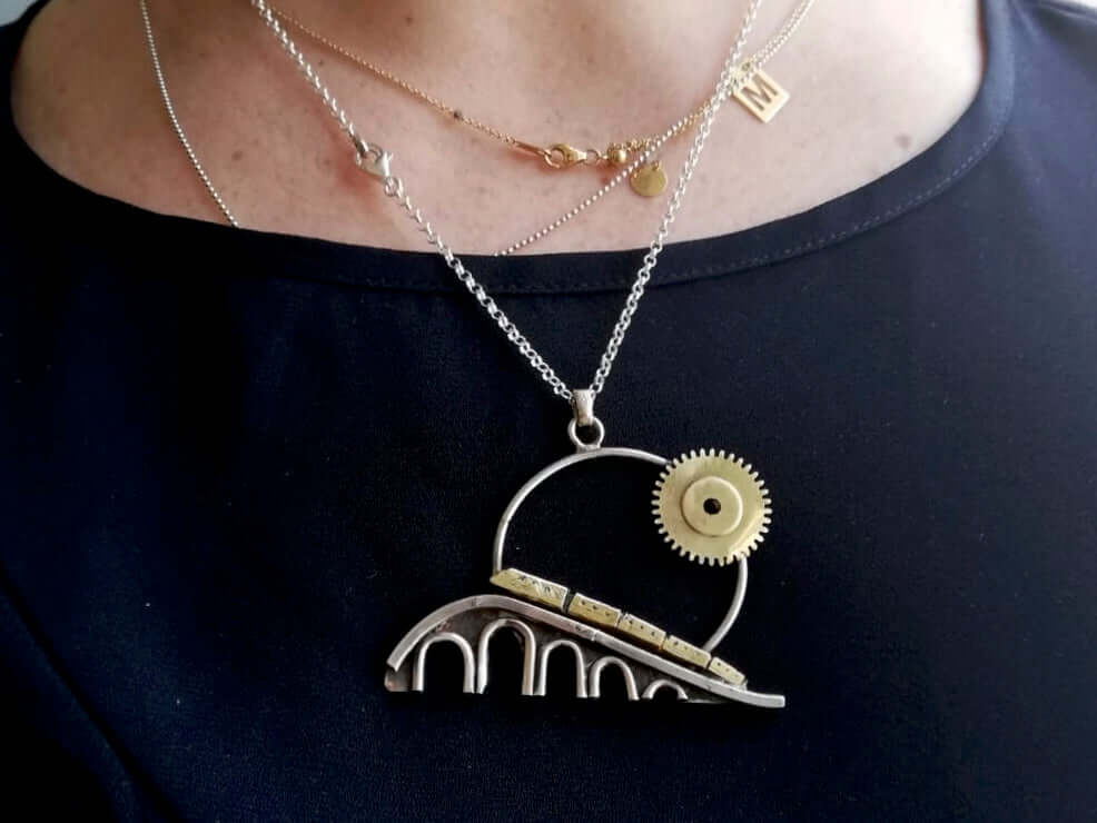 Collana artigianale treno ponte con design a ingranaggi da Glimoire indossata su collo femminile