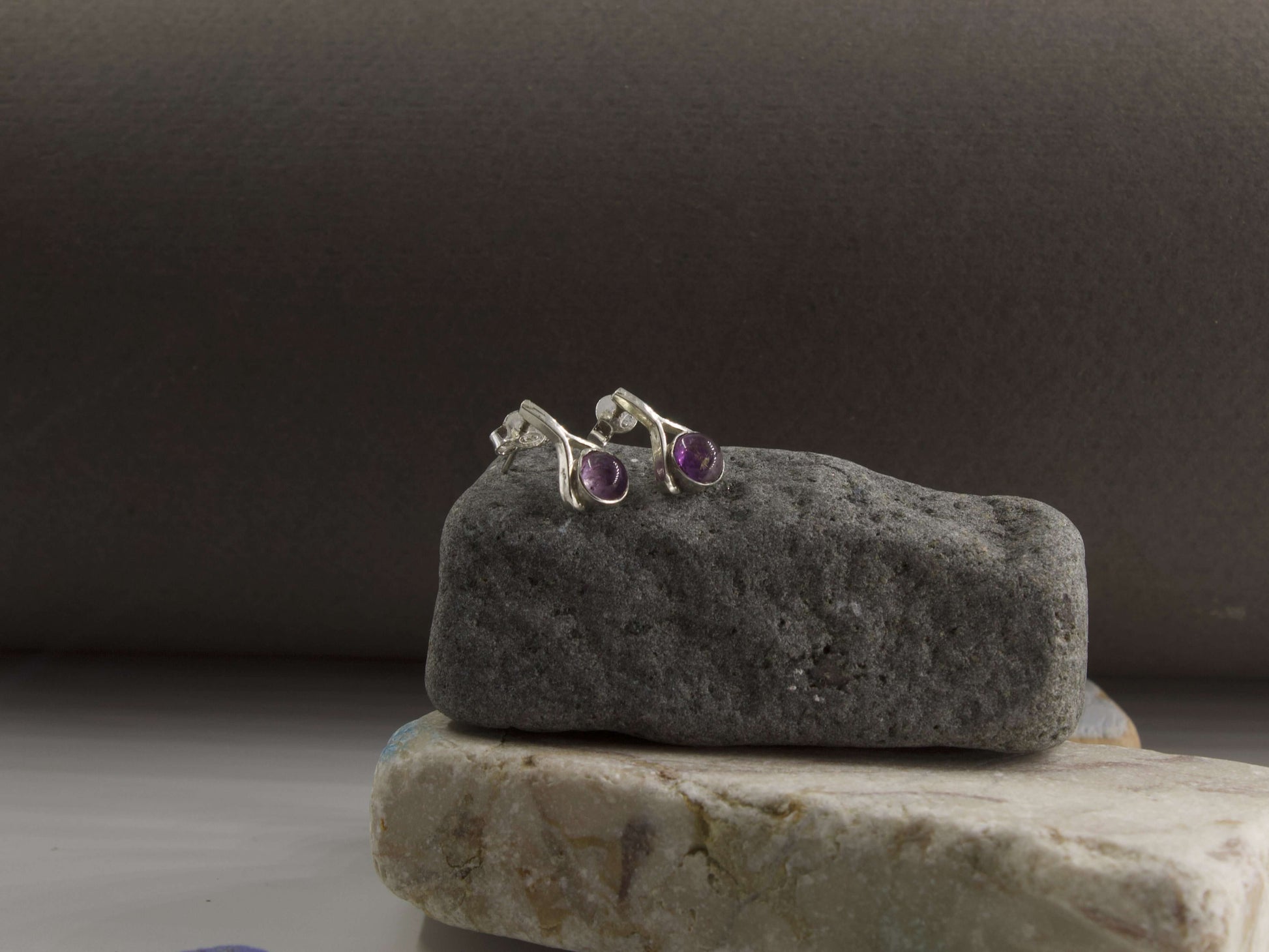 Orecchini a goccia pietra blu Glimoire con montatura in metallo su sfondo naturale di pietre