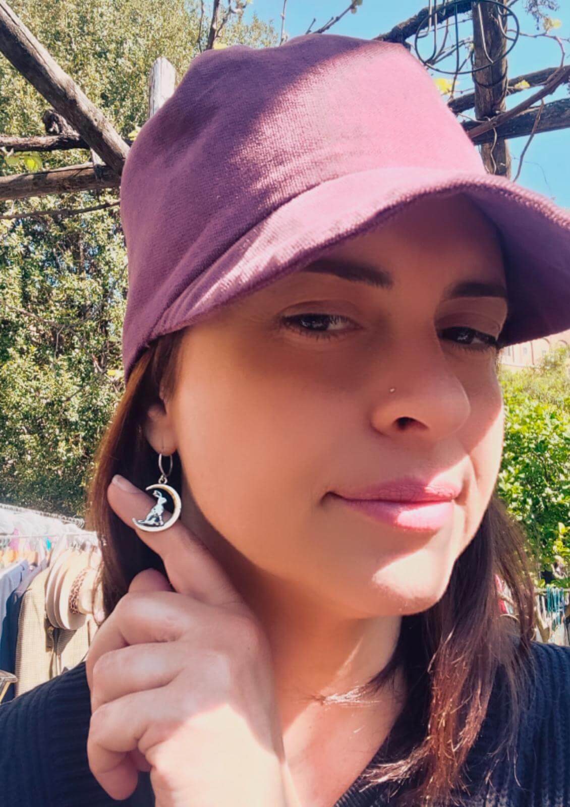 Gli orecchini artigianali lepre luna indossati da una donna con un cappello, in dettaglio, sullo sfondo verde