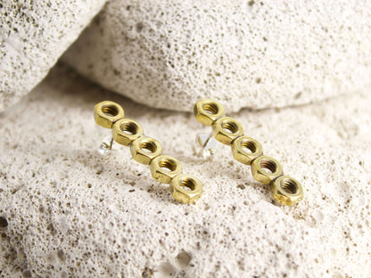 Orecchini esagonali dadini in ottone con design moderno su sfondo roccioso