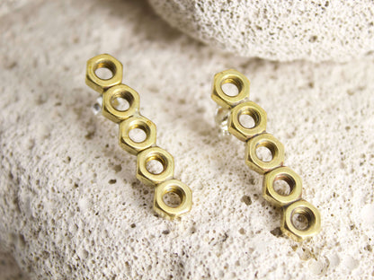 Orecchini esagonali dadini in ottone con design moderno su sfondo di pietra naturale