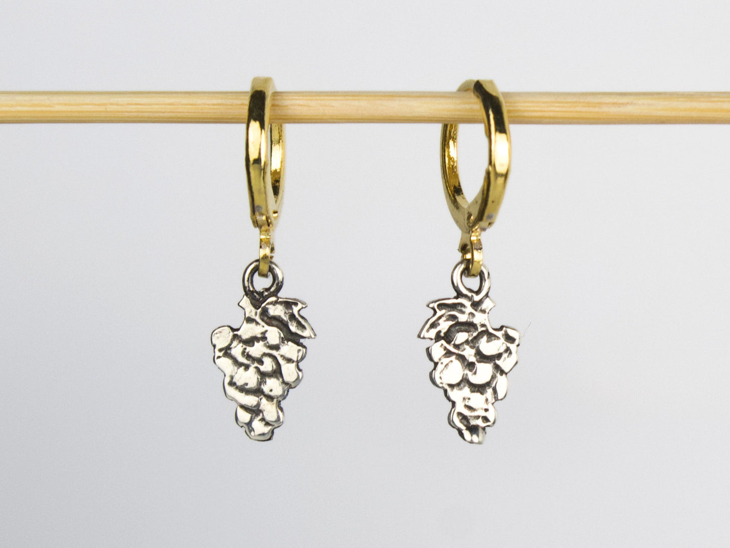 Orecchini a lobo di Glimoire con charm a forma di grappolo d'uva in argento e cerchietti in ottone dorato.