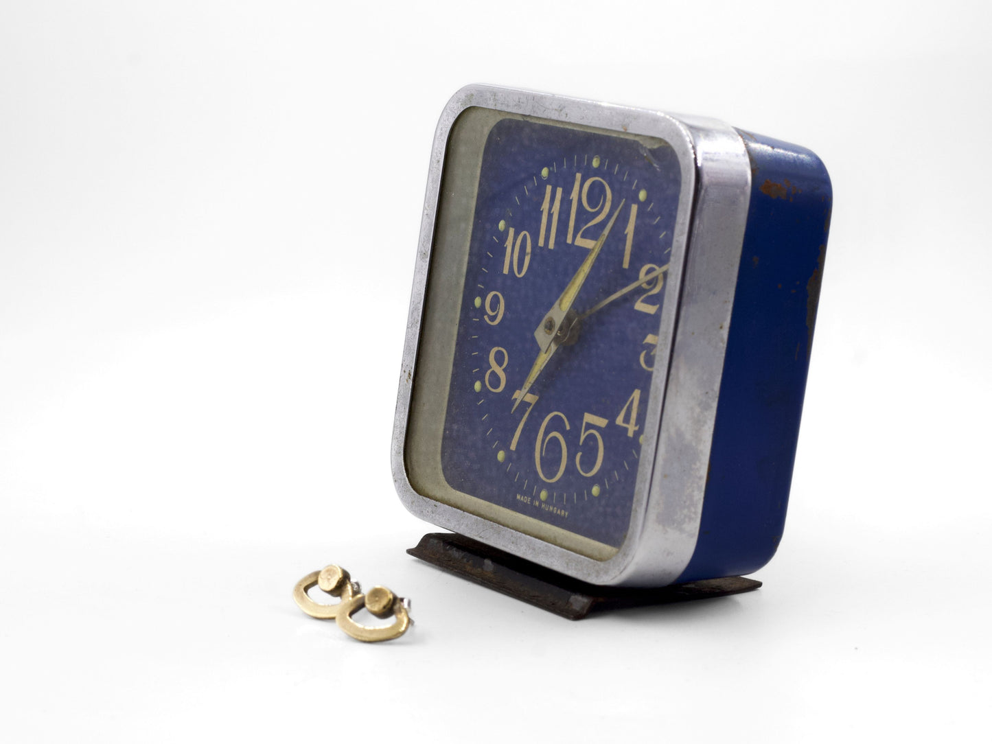 Orecchini particolari ispirati a sveglie accanto a una sveglia vintage blu con quadrante bianco