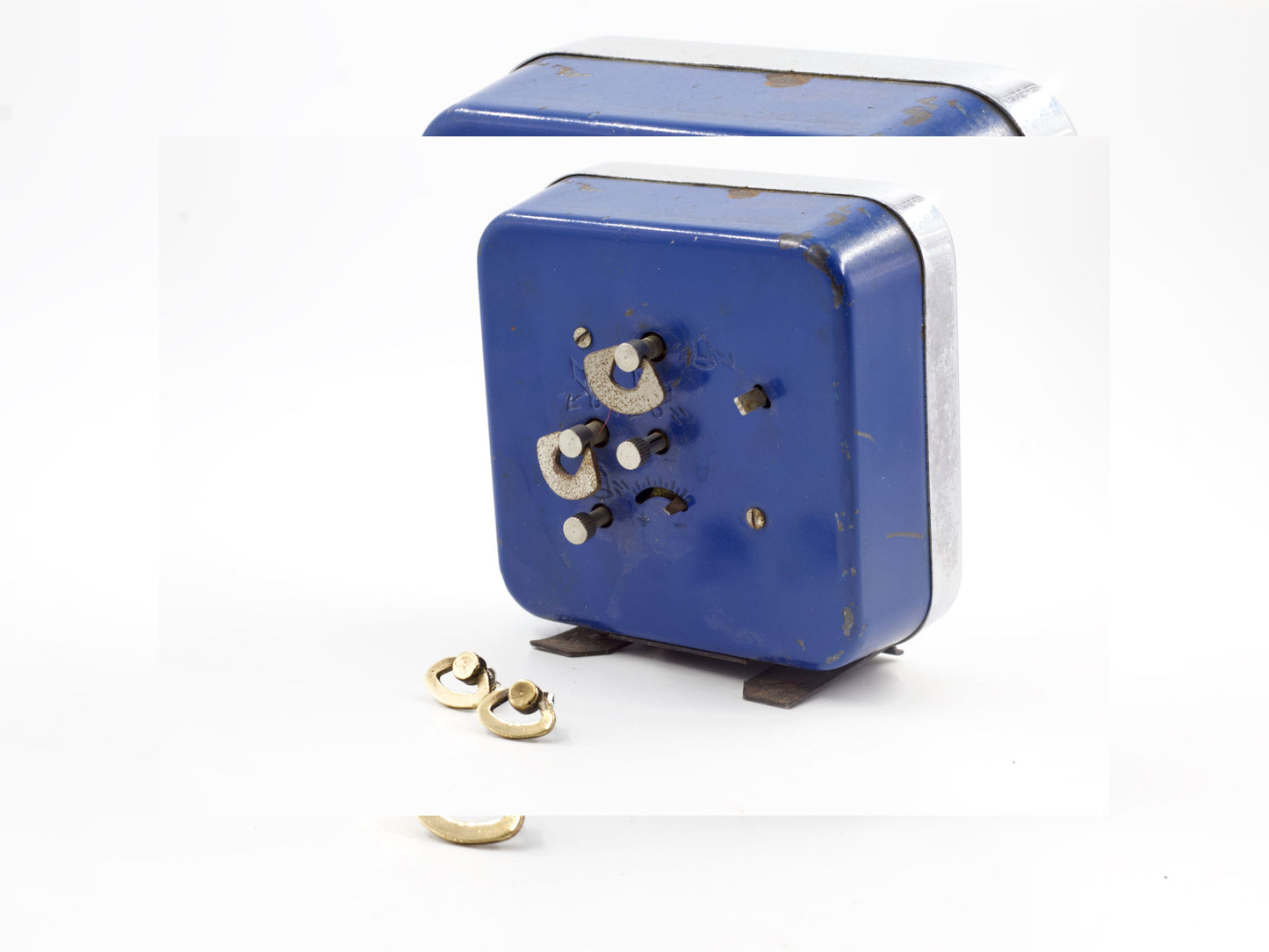 Orecchini particolari ispirati a sveglie con dettagli dorati accanto a una sveglia blu vintage