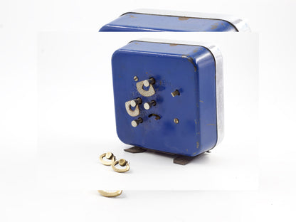 Orecchini particolari ispirati a sveglie con dettagli dorati accanto a una sveglia blu vintage