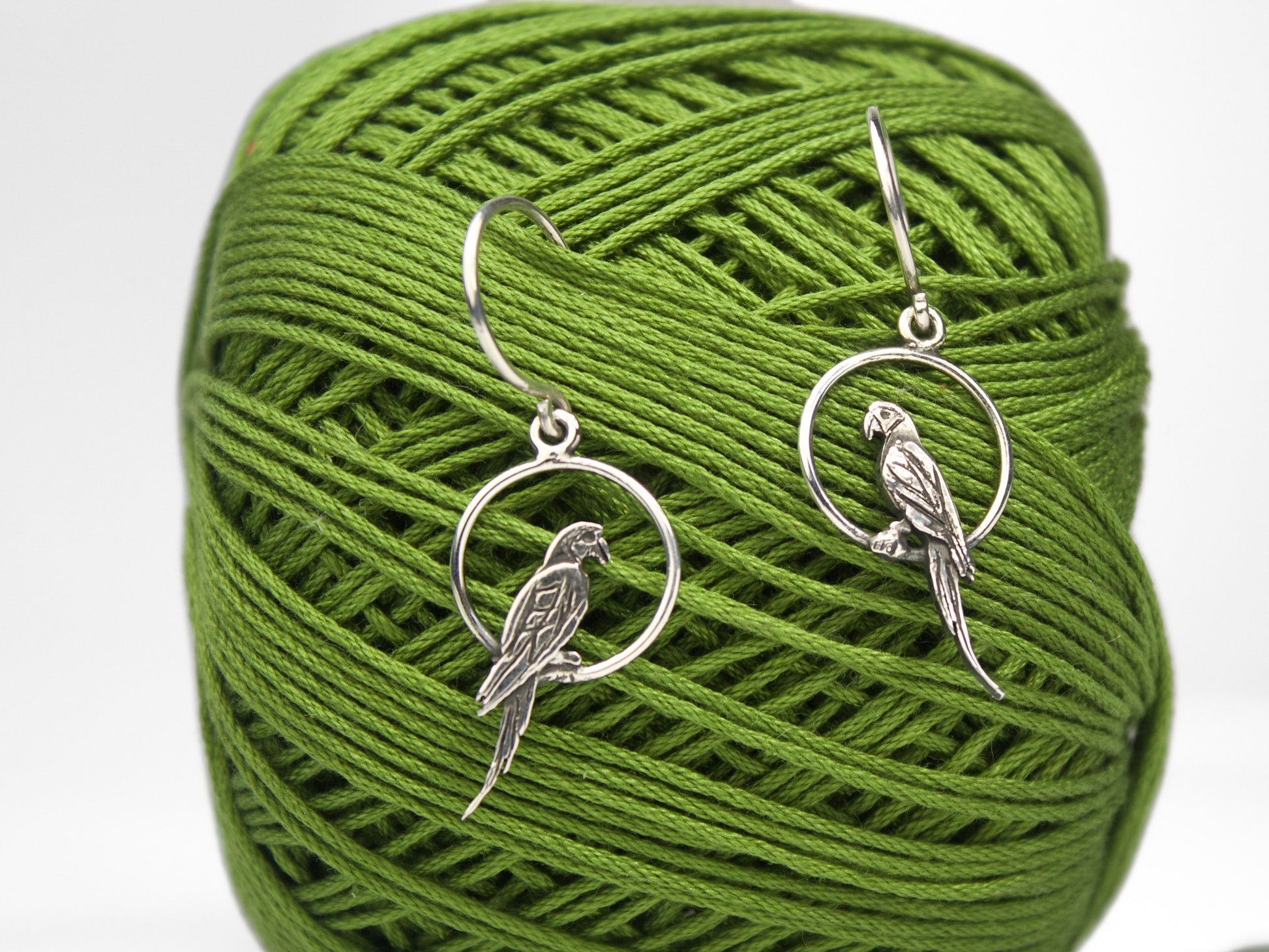 Orecchini Pappagallini - Serie Minimali in argento, con incisioni a mano e cerchi argentati, appesi su un gomitolo di filo verde.
