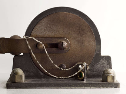 Collana Glimoire con pendente ingranaggi pietra verde su sfondo metallico industriale