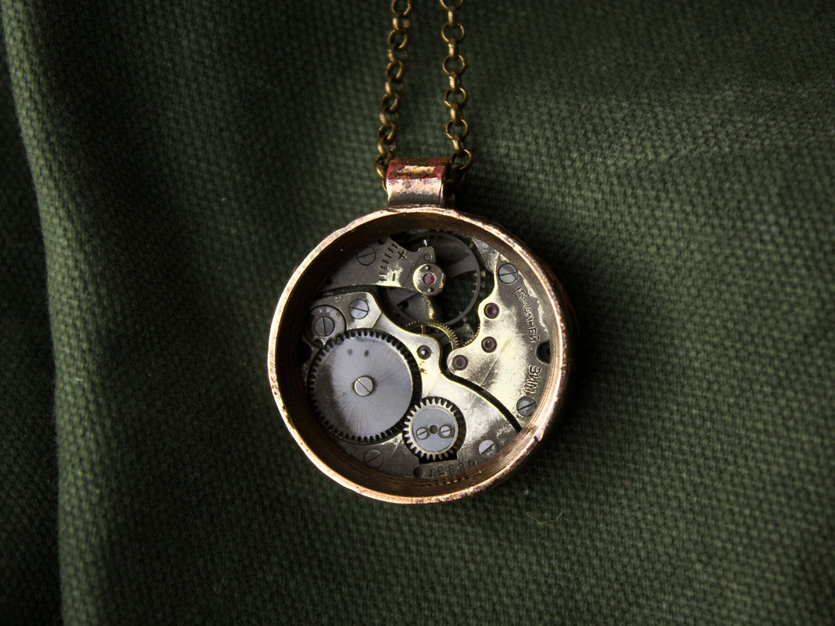 Collana in ottone con pendente rotondo, che mostra un meccanismo di orologio in bronzo con dettagli bruniti e lucidi.